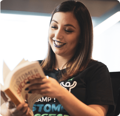 Uma mulher sorridente e com cabelo de cor castanho está folheando o livro Customer Success do autor Dan Steinman.
