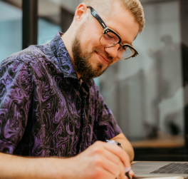 Um homem veste uma camisa de cores preta e roxo segura um descatador de textos fazendo anotações.